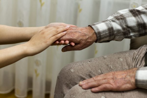 Seated elderly mans hands being held by younger woman's hands